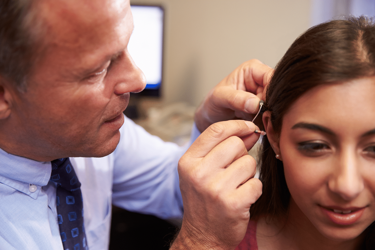 Audiologist fitting younger woman with hearing aids
